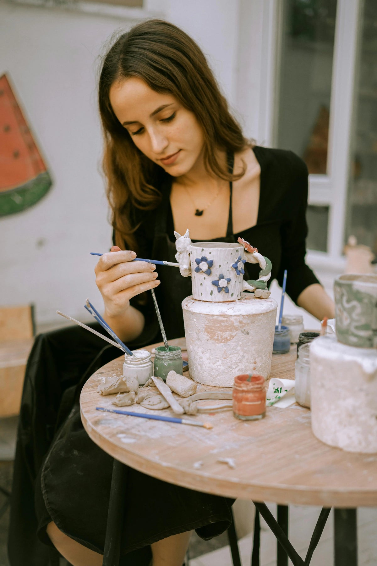 Gemeinsame Töpfer-Session mit Freunden: Frau verziert Keramikbecher mit DIY-Töpferset und Pinsel.